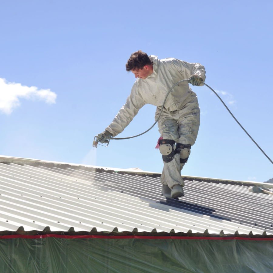 A trademan uses an airless spray to paint the roof of a building